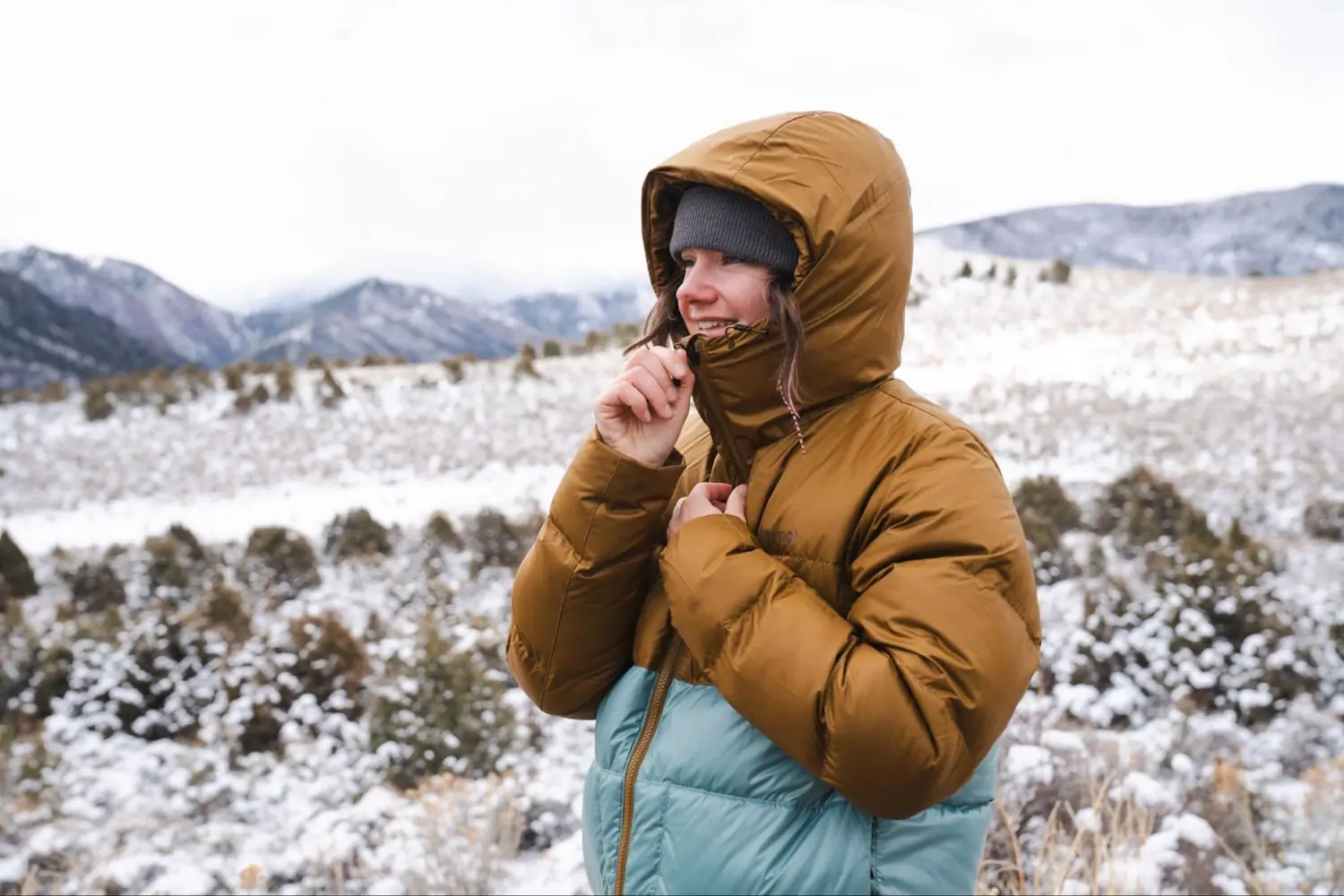 Bundled up in a Marmot Guide Hoody, a woman adjusts her hood in a snowy mountain scene