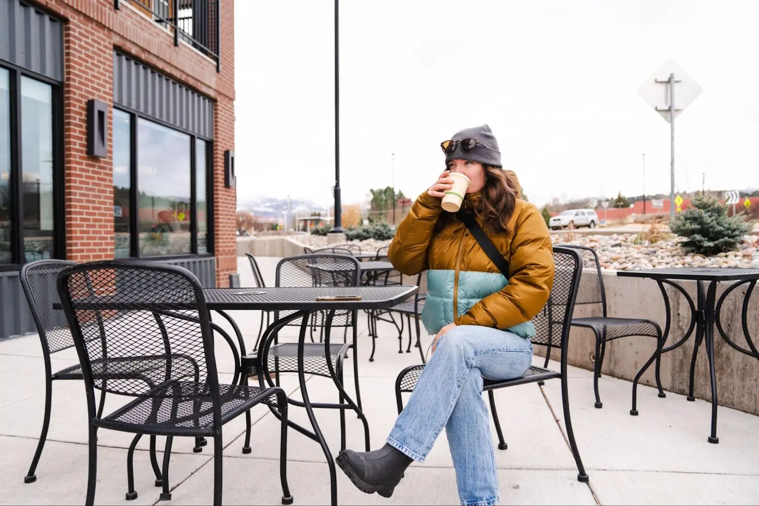 Woman in a brown and teal Marmot Guide Hoody sitting at an outdoor cafe, drinking a hot beverage