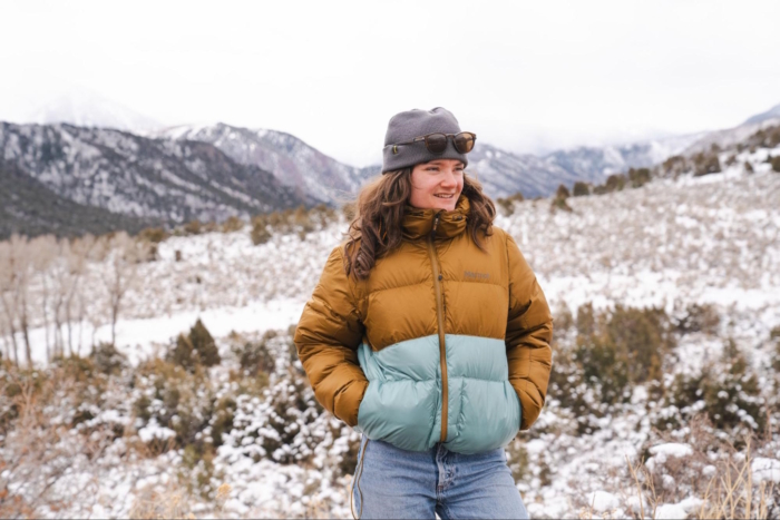 Woman in brown and teal puffer jacket standing in a snowy mountain landscape,