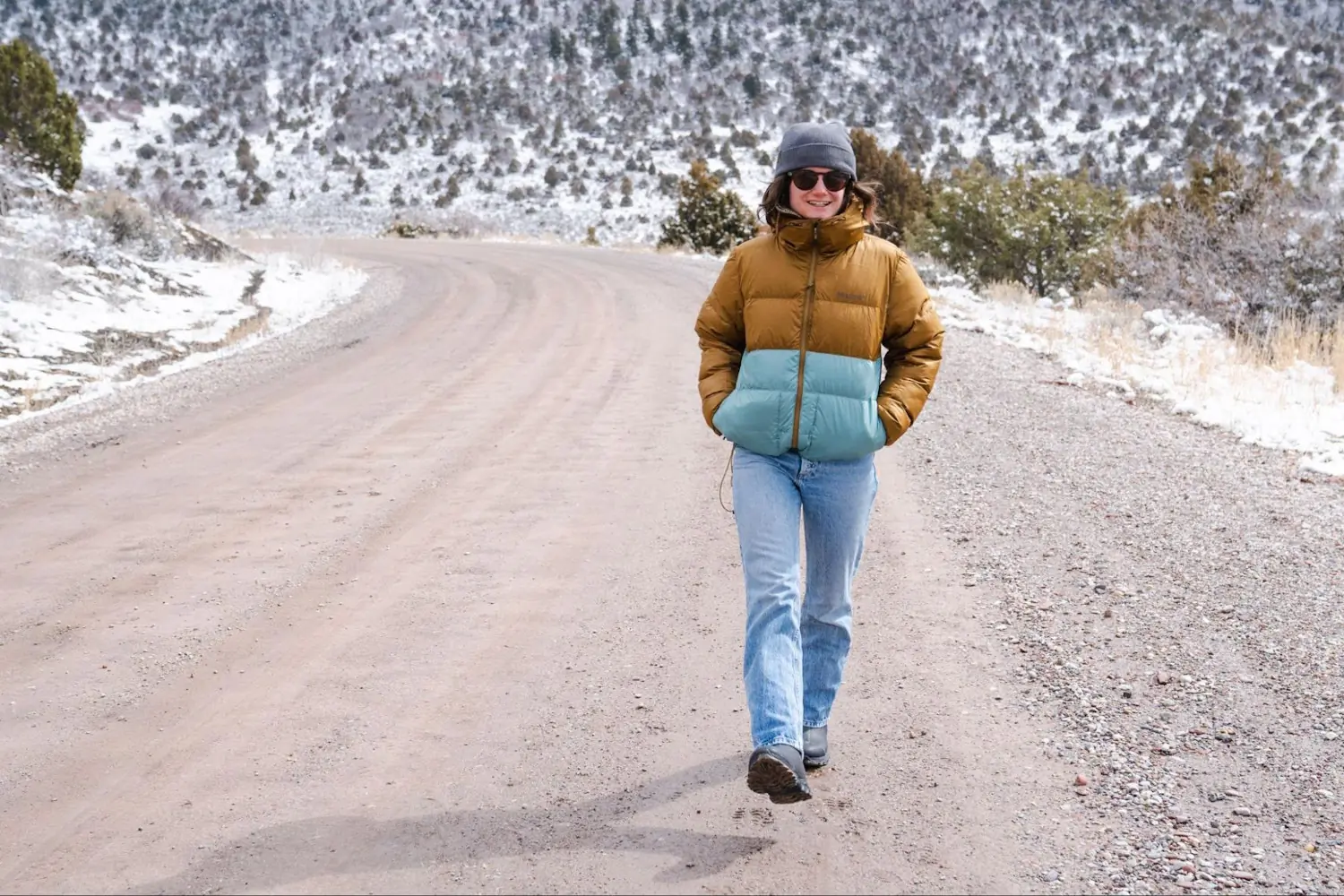 Woman wearing a puffer jacket walking on a scenic, snowy mountain road