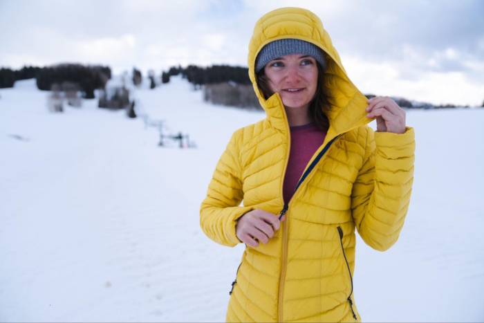 Woman wearing decathlon forclaz jacket, standing in a snowy landscape and adjusting the jacket's zipper