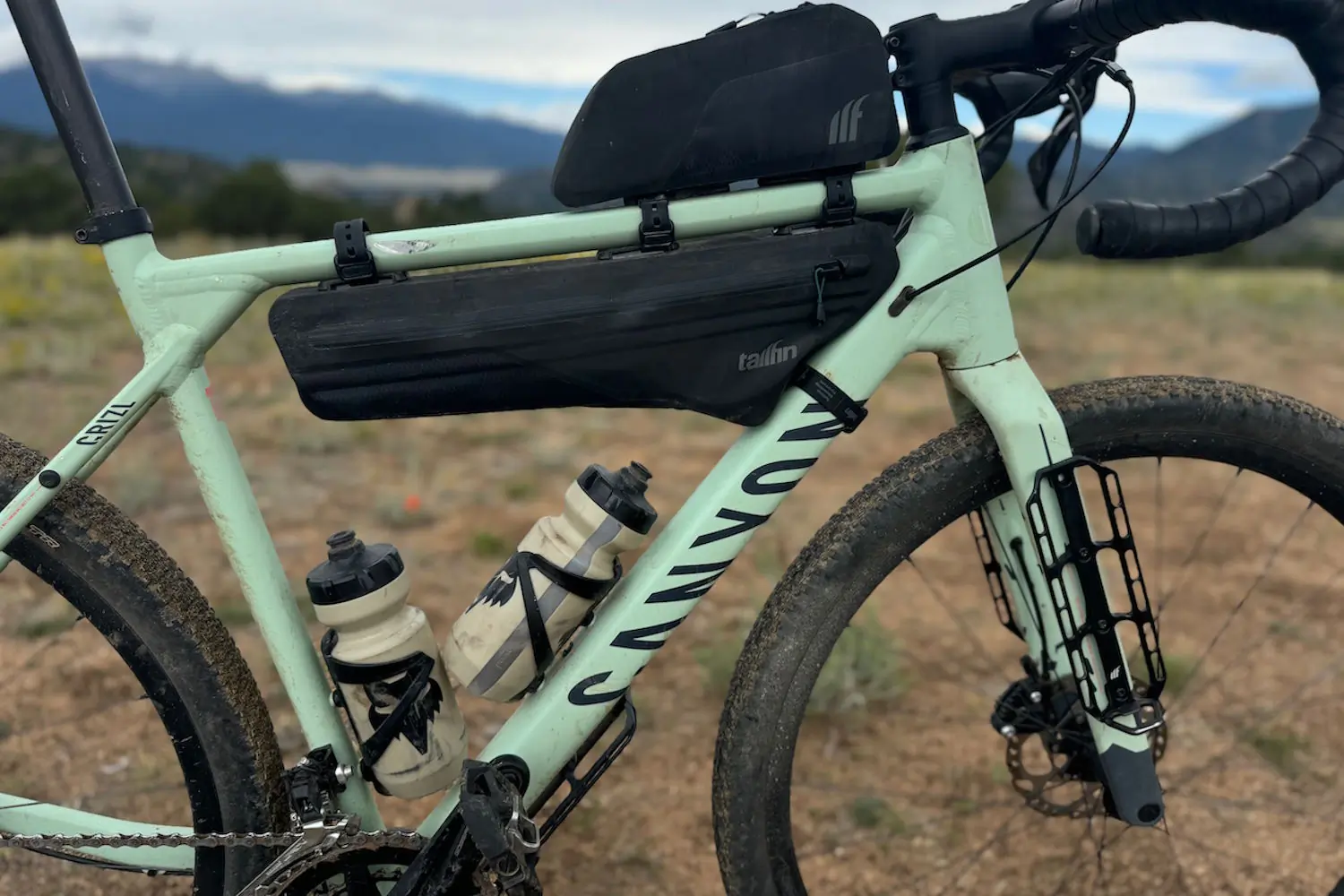 A light green gravel bike equipped with Tailfin frame bags and two water bottle