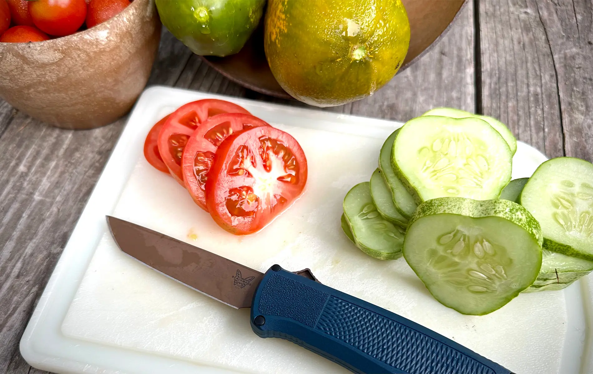 benchmade shootout otf knife next to the sliced tomatoes and cucumbers on a cutting board