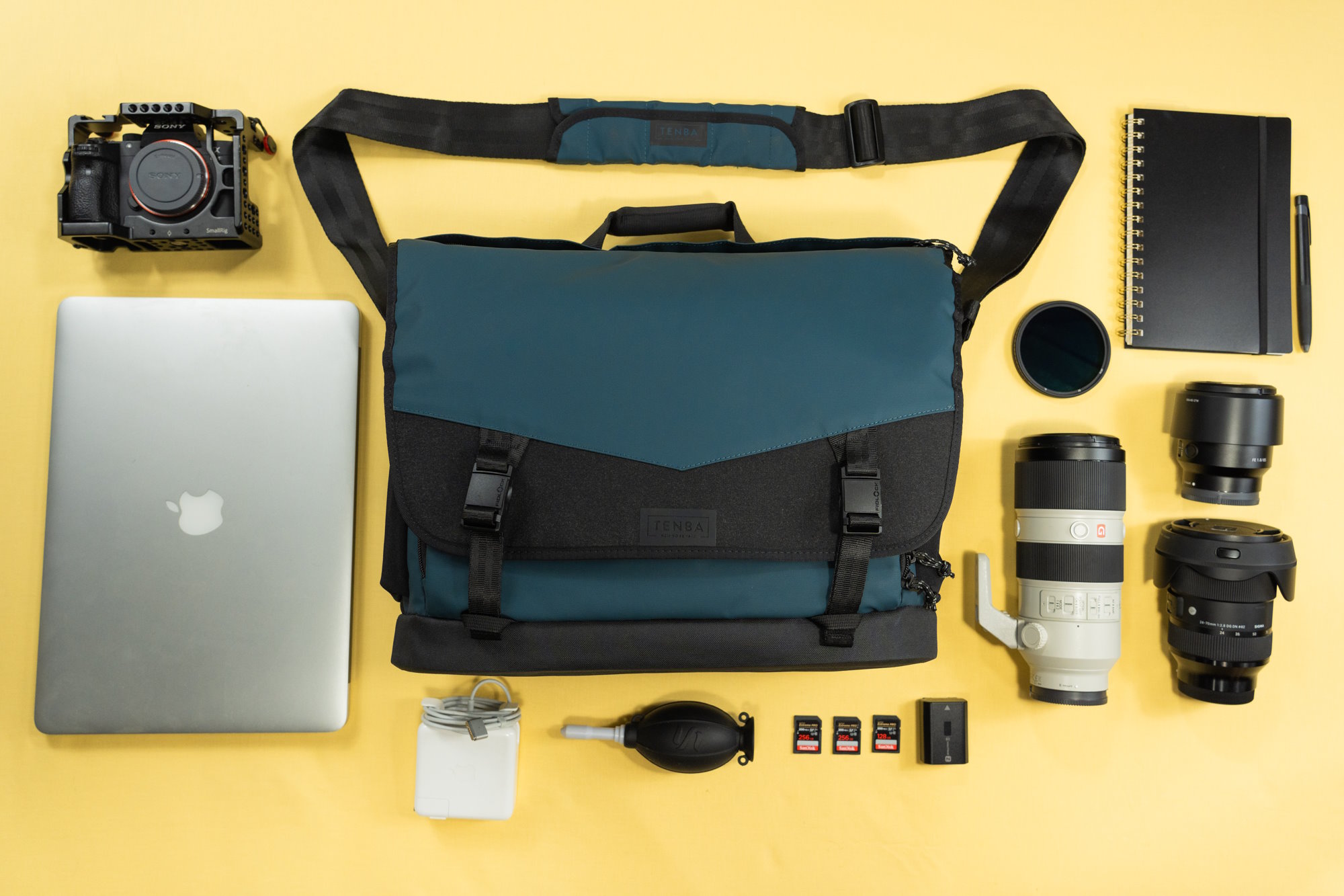 A flat lay of camera gear, including lenses, a MacBook, a camera, and accessories