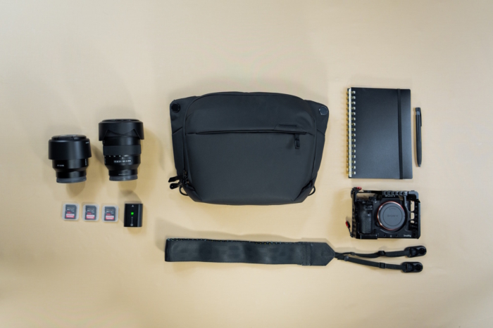 Flat lay of photography gear including a sling bag, camera, and various photography accessories