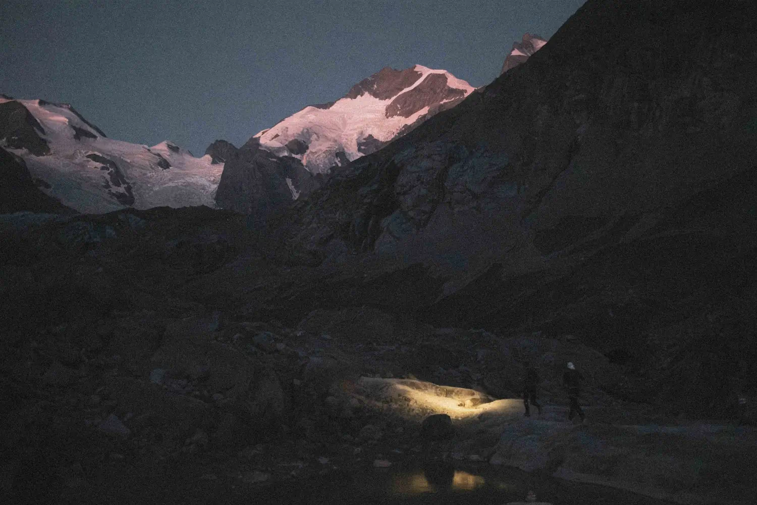 Two people with headlamps walk across a rocky landscape at night