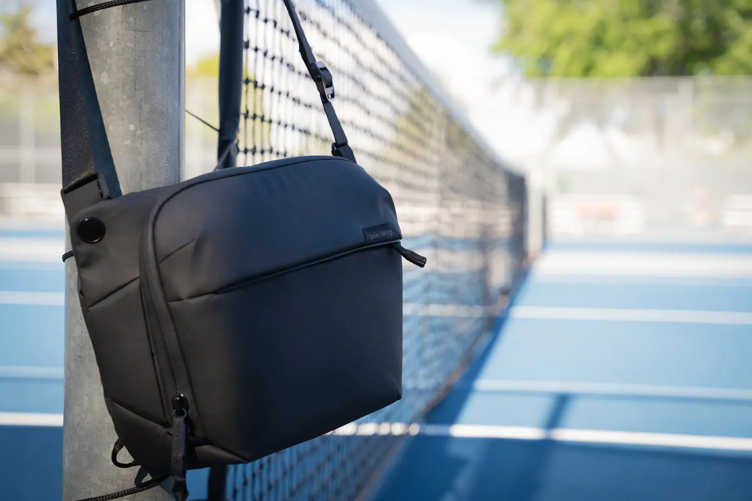 Peak Design sling bag hanging on a tennis court fence