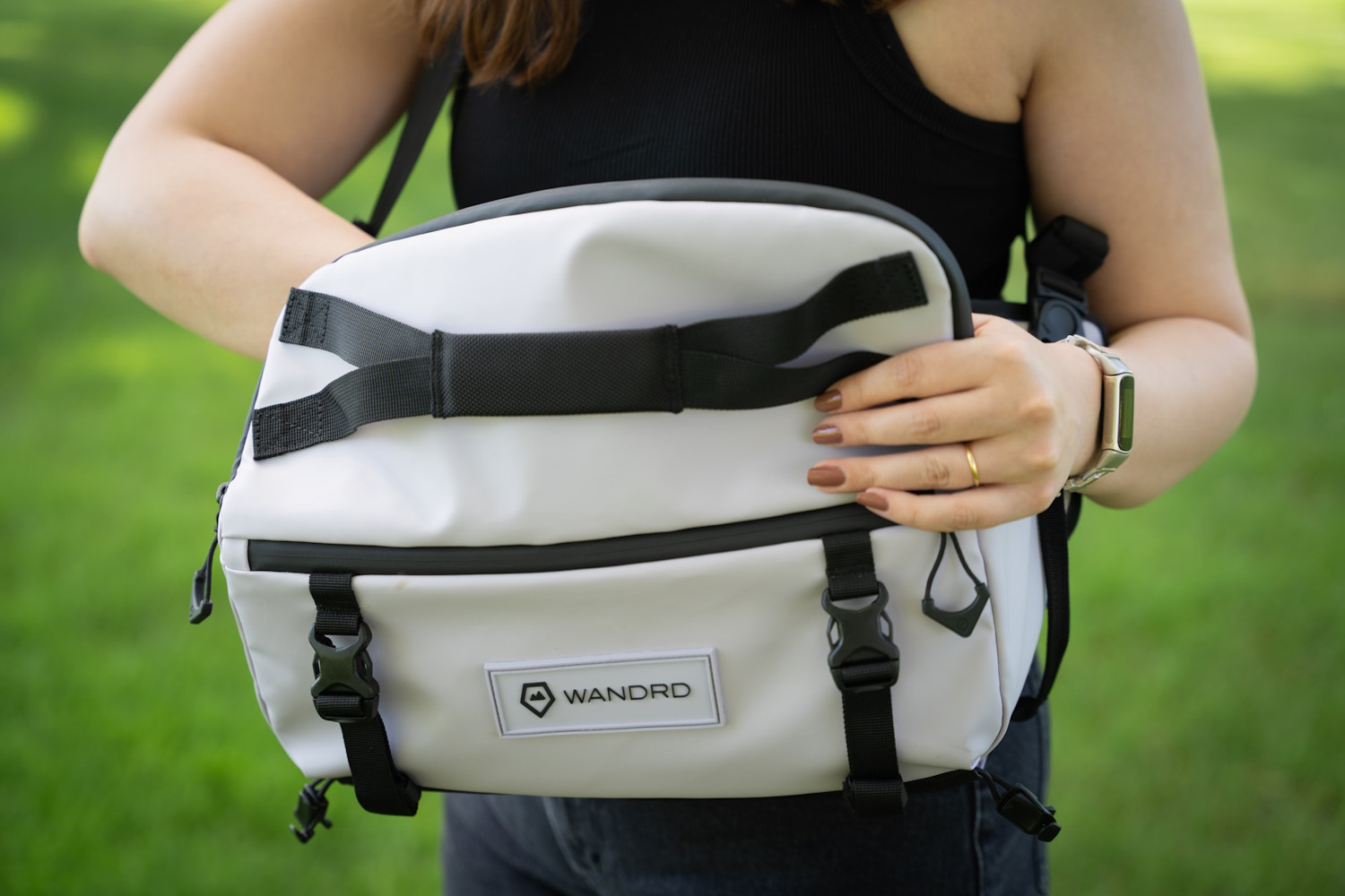 Person holding a WANDRD Rogue Sling camera bag outdoors with a grassy background, showcasing the bag's design and straps