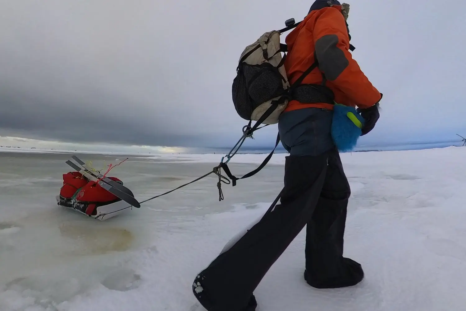 Person in winter gear pulling a sled across a frozen landscape