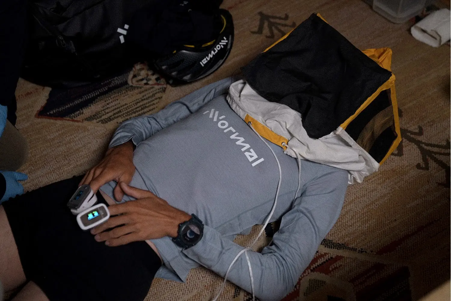 A person lying on the floor with a pulse oximeter on their finger and a bag over their head