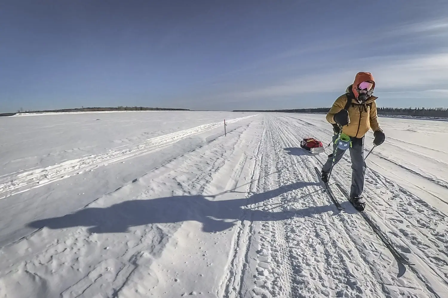 A skier pulls a sled across a vast, snowy landscape under a clear blue sky
