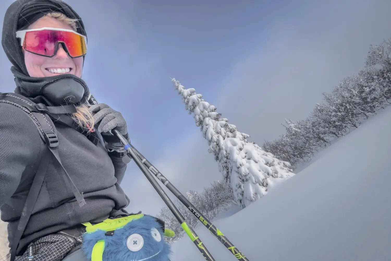 Sunny Stroeer smiling in winter gear holds ski poles, standing in a snowy landscape