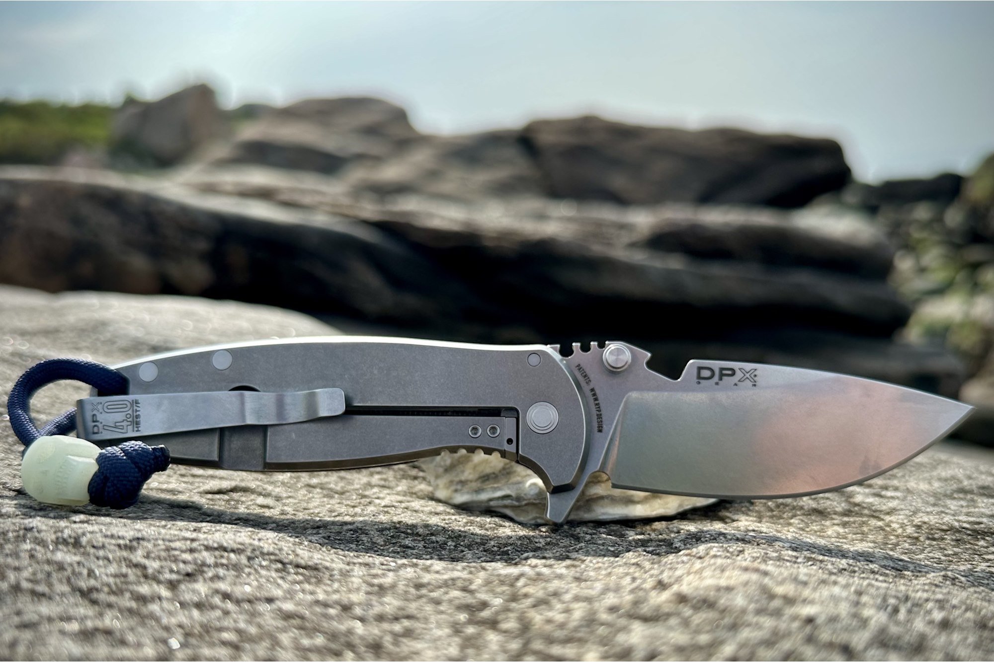A DPx Gear HEST/F 4.0 folding knife lies open on a rock