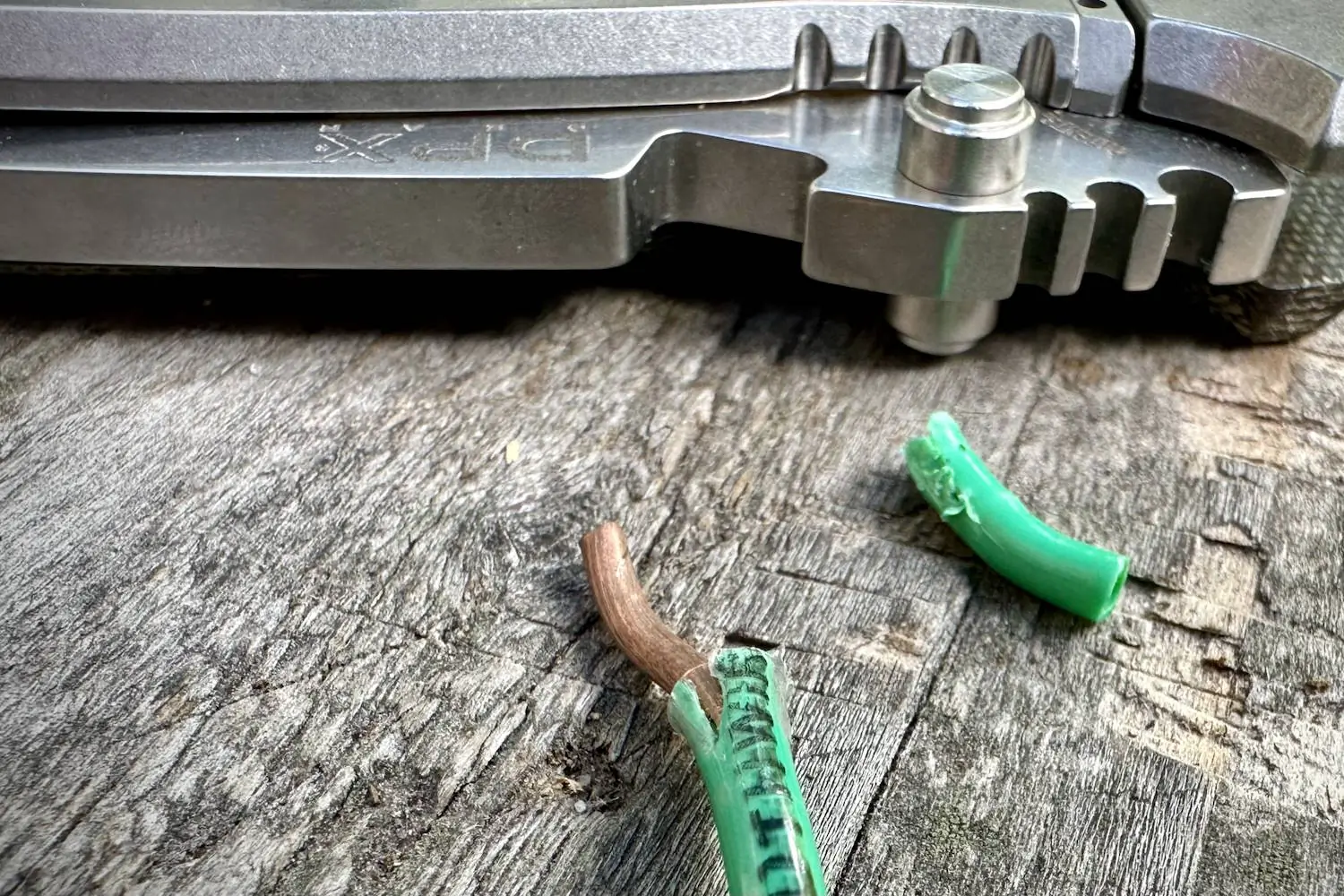 Close-up of the DPx Gear HEST/F 4.0 knife on a wooden surface, with a green electrical wire