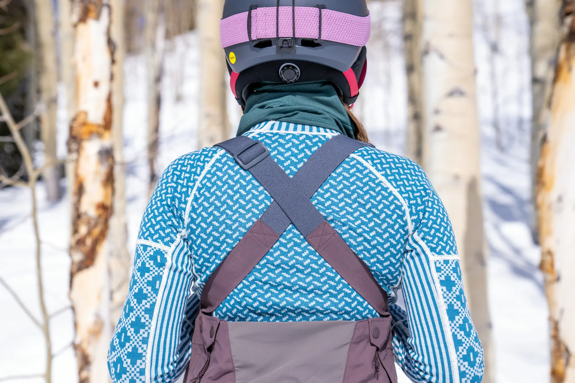 woman facing away from camera with base layer top and ski bibs on