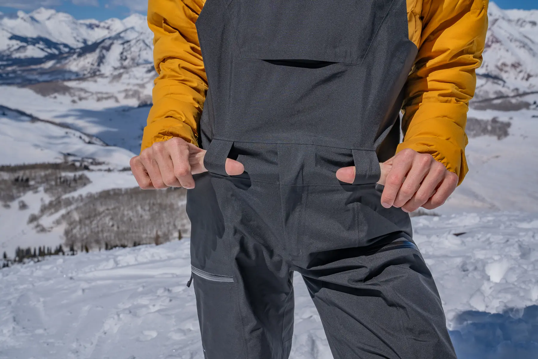 man putting thumbs into belt loops on ski bibs 