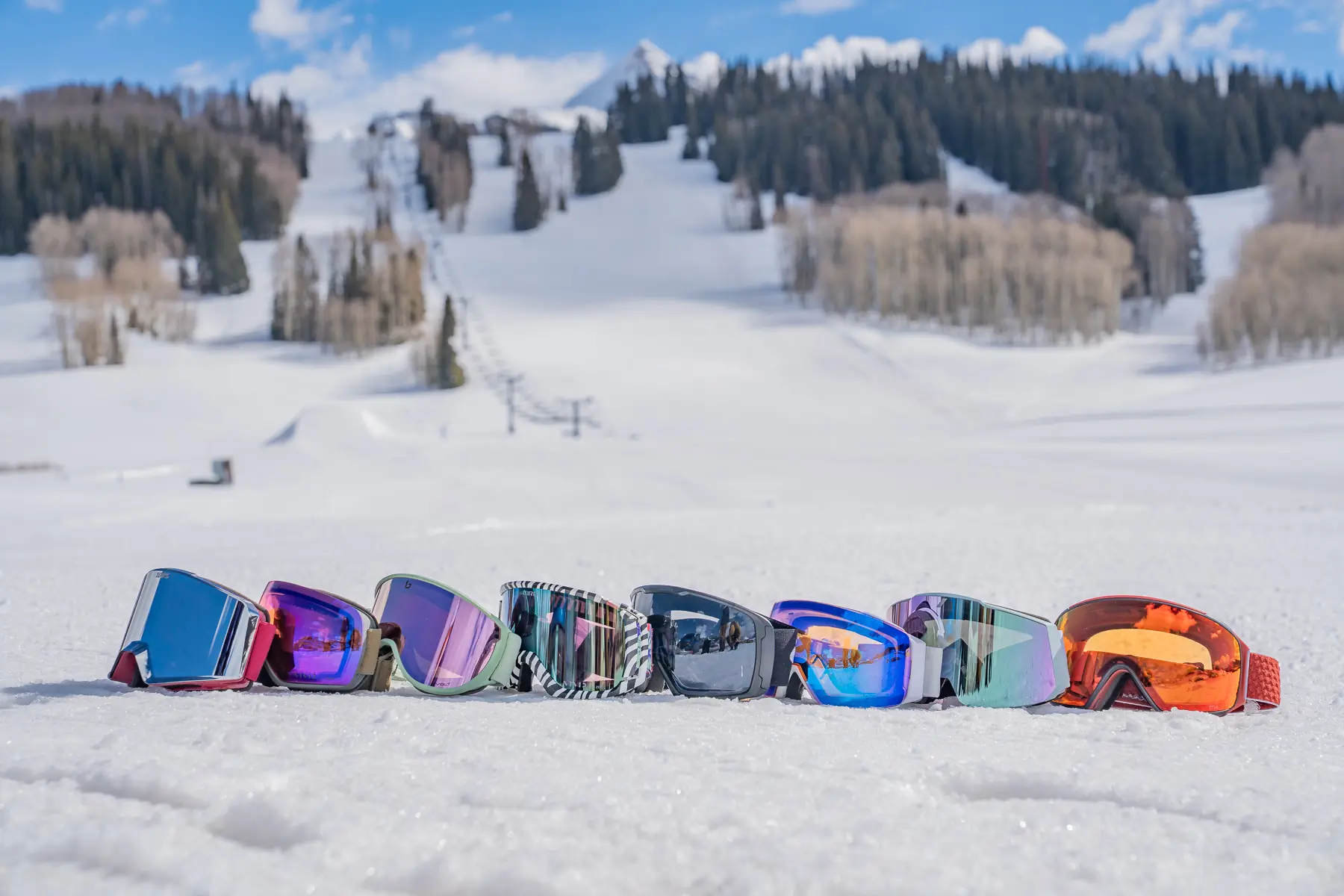 a lineup of snow goggles with the ski area backdrop 