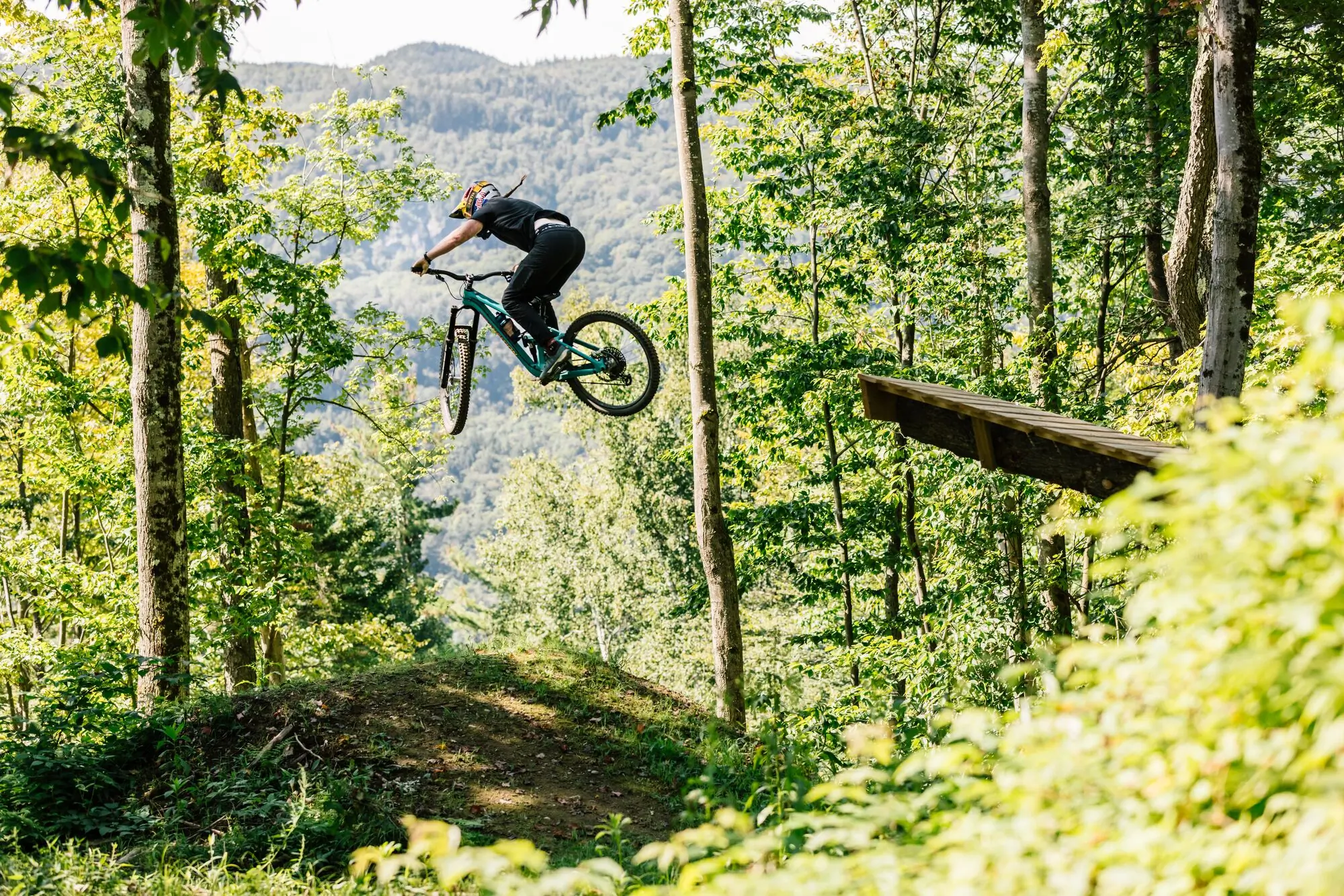 A mountain biker jumping on a feature in a wooded area.