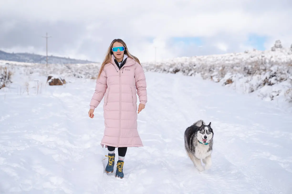 woman walking in calf-length winter jacket with Husky dog