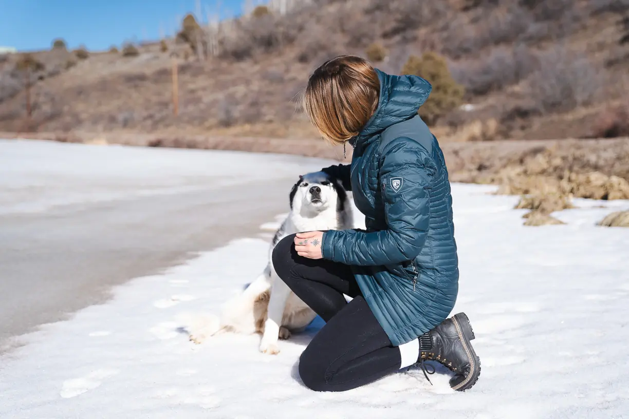 woman kneeling with husky while wearing 800-fill down jacket 