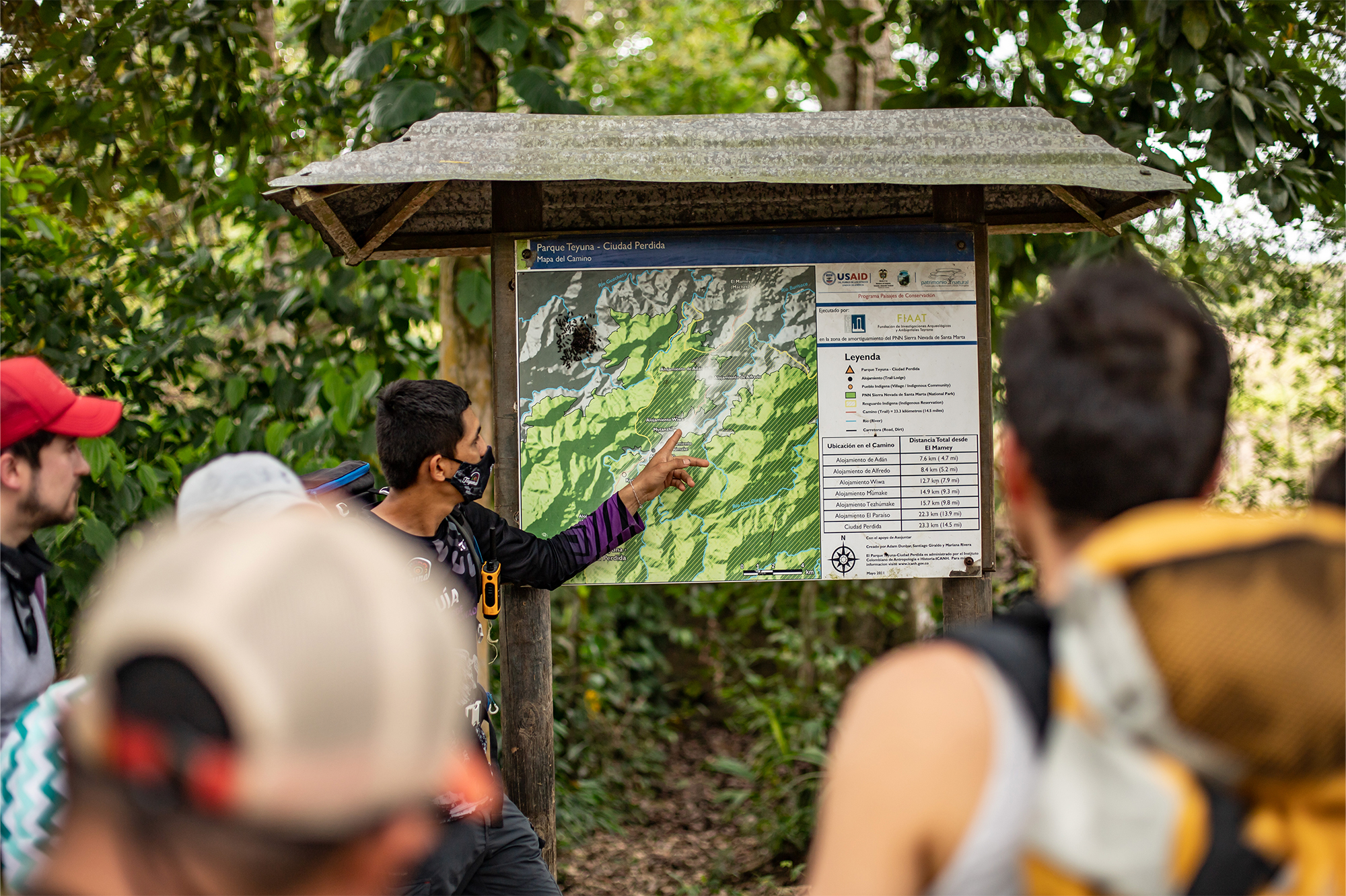 a tour guide stands in front of a trail map, pointing to path