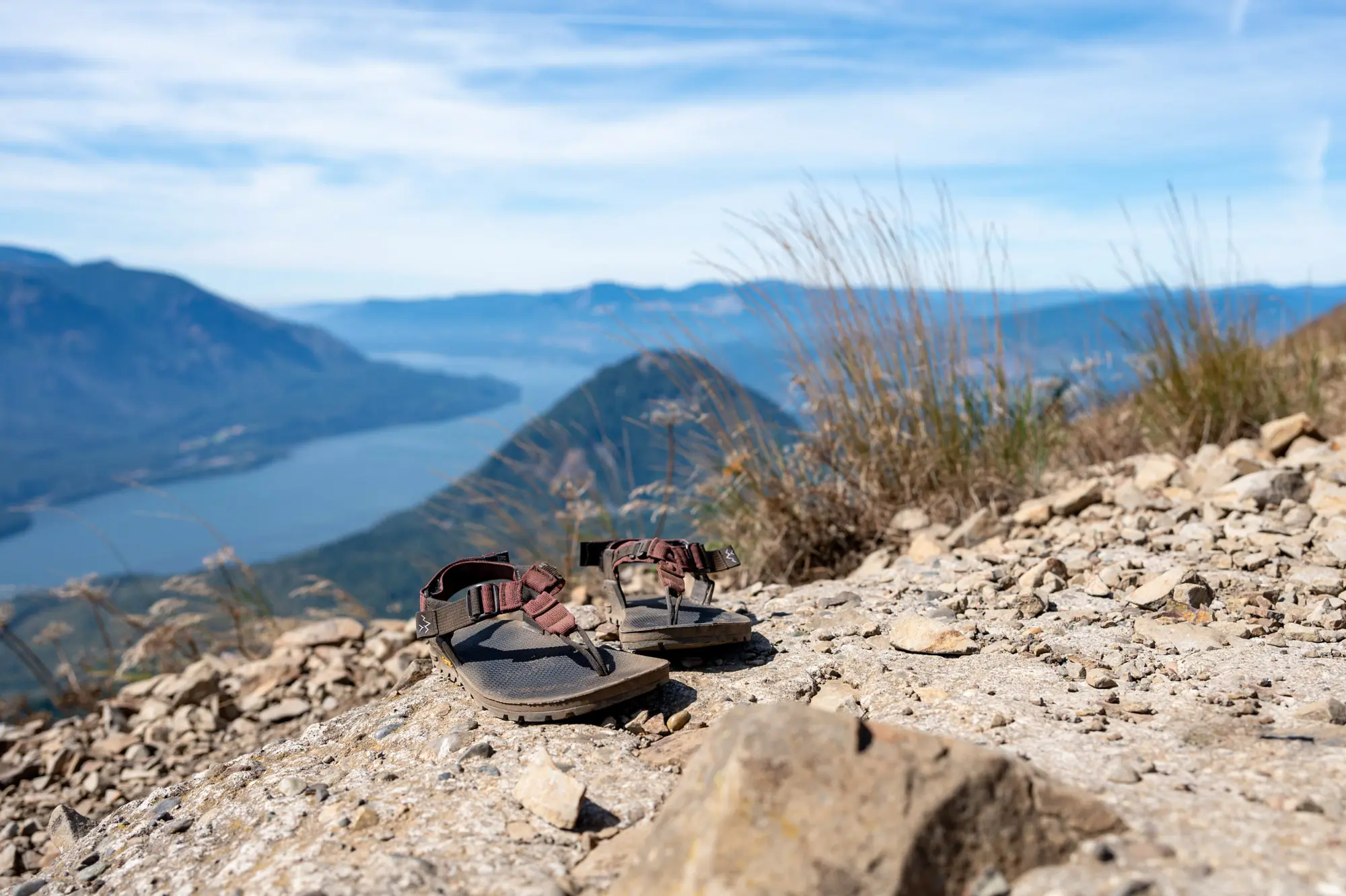 the bedrock cairn evo sandals sit on a trail high above a lake