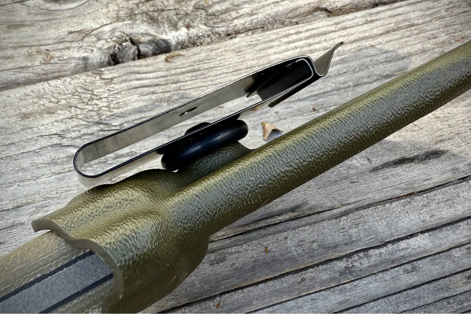 A close-up of a belt clip attached to a green knife sheath