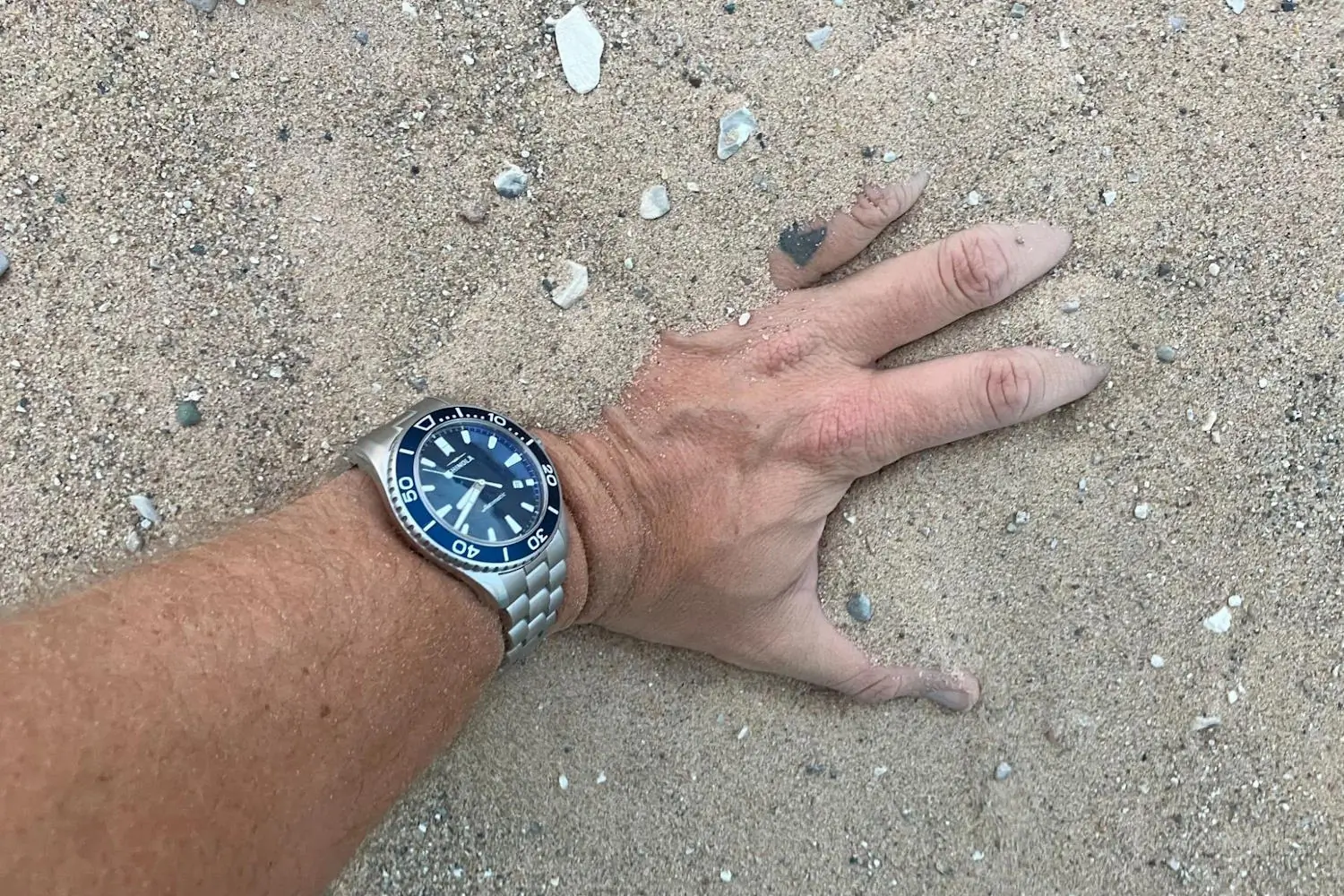 A hand partially buried in sand wearing a Lake Michigan monster watch