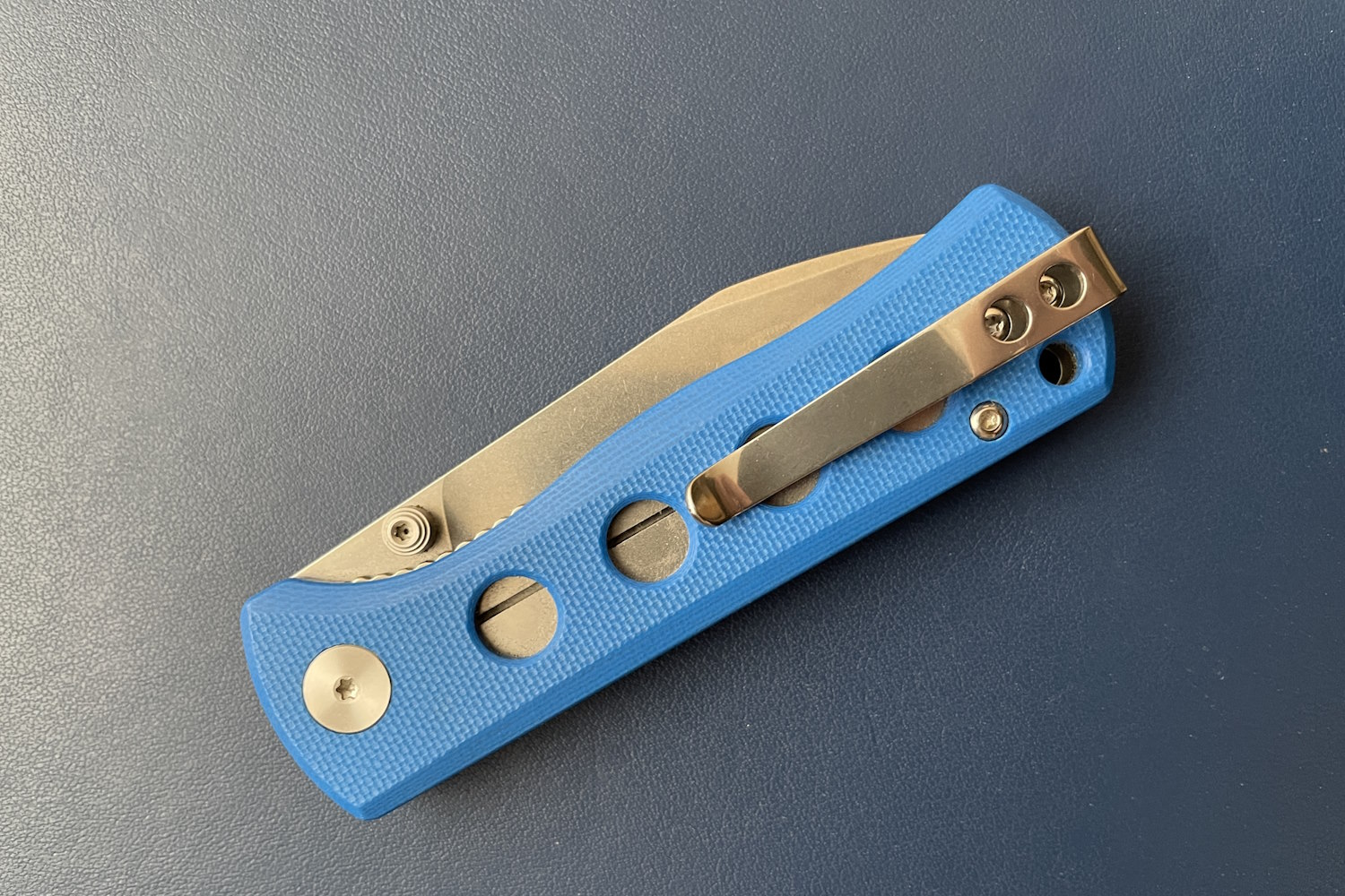 Qanary knife closed with a blue handle and circular cutouts, showing the metal pocket clip on the back