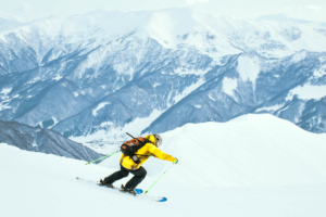 Close up dynamic sports banner of man skier on piste ski downhill fast motion in Alps. Active winter holidays, skiing downhill in overcast day. Ski rides on the track with swirls of fresh snow