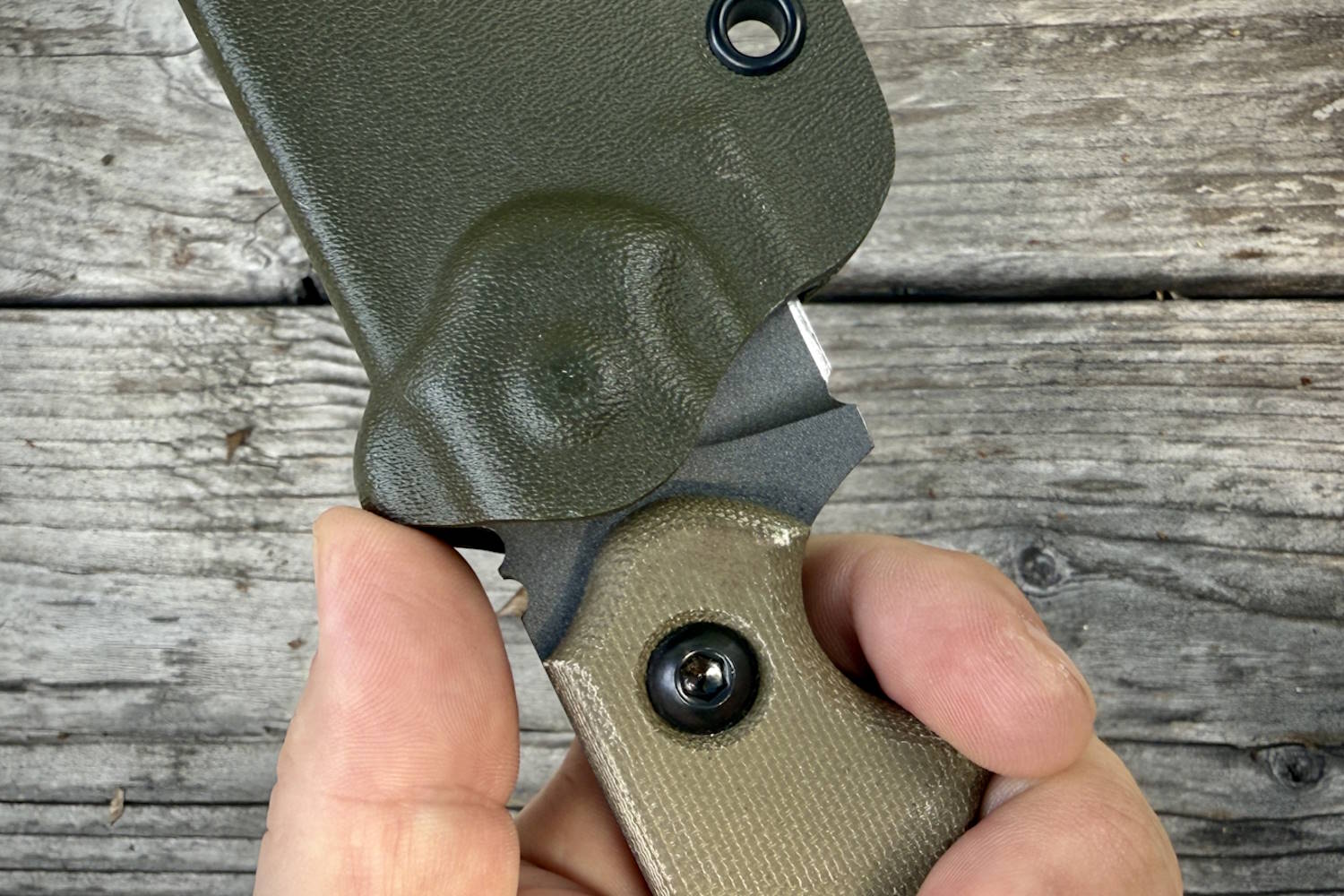 A close-up of a hand holding a knife with a green sheath, showing the thumb ramp