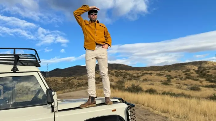 the author wears the western rise evolution 2 travel pants while standing on the hood of a classic landrover