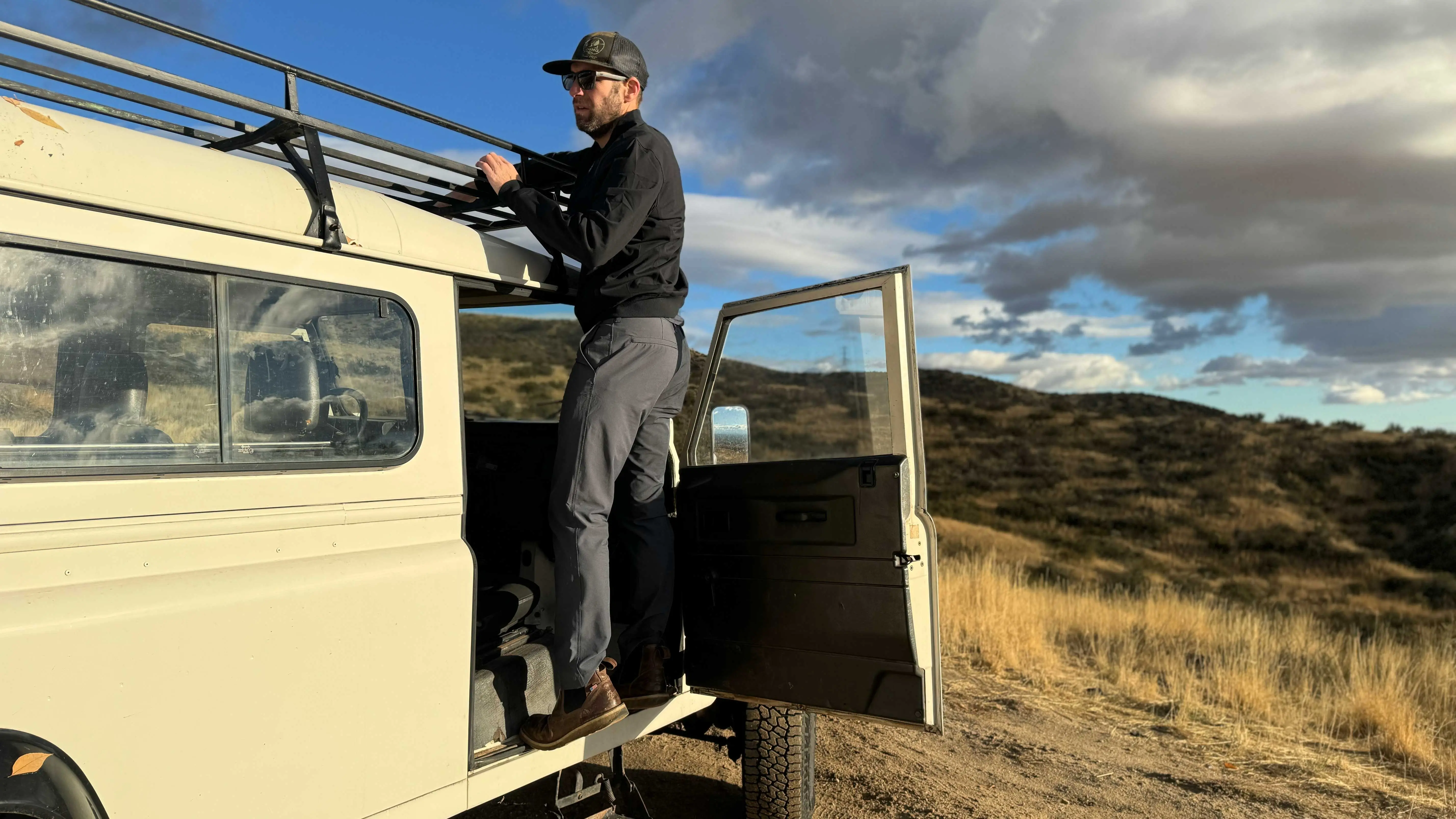 the author packs gear onto the roof rack of a classic landcruiser while wearing the envoy lighweight pants