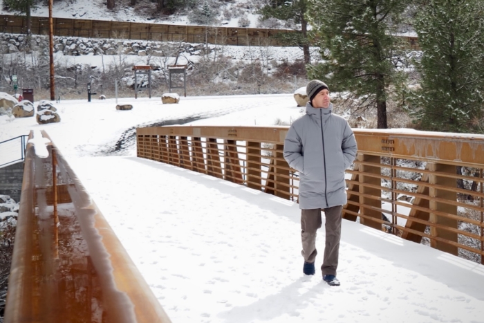 A handsome, middle-aged man walking across a snowy footbridge in Truckee, Calif., wearing the Patagonia Jackson Glacier Parka.