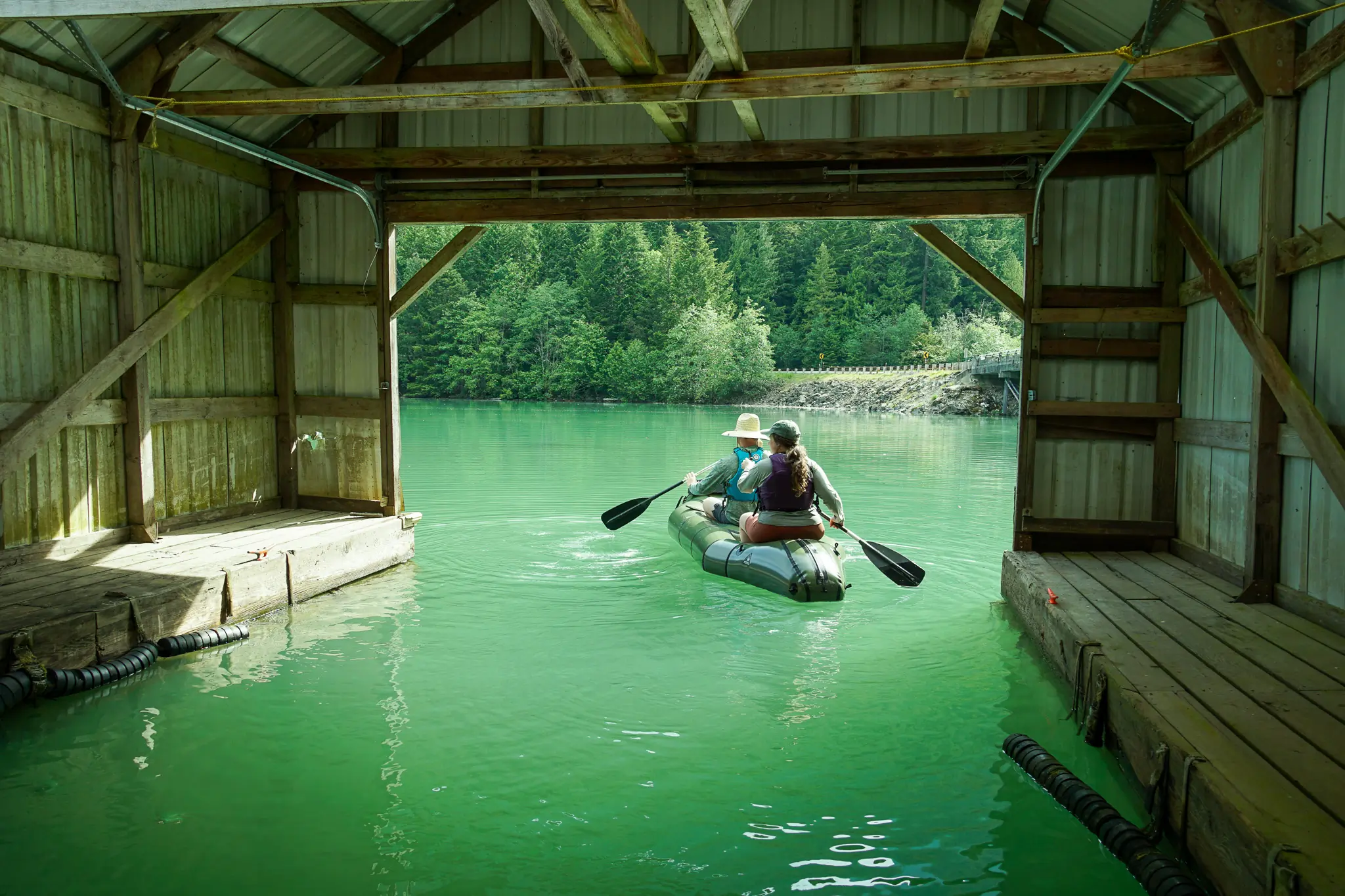 two paddlers in the rendezvous paddle out of a floating boathouse on diablo lake in the north cascades
