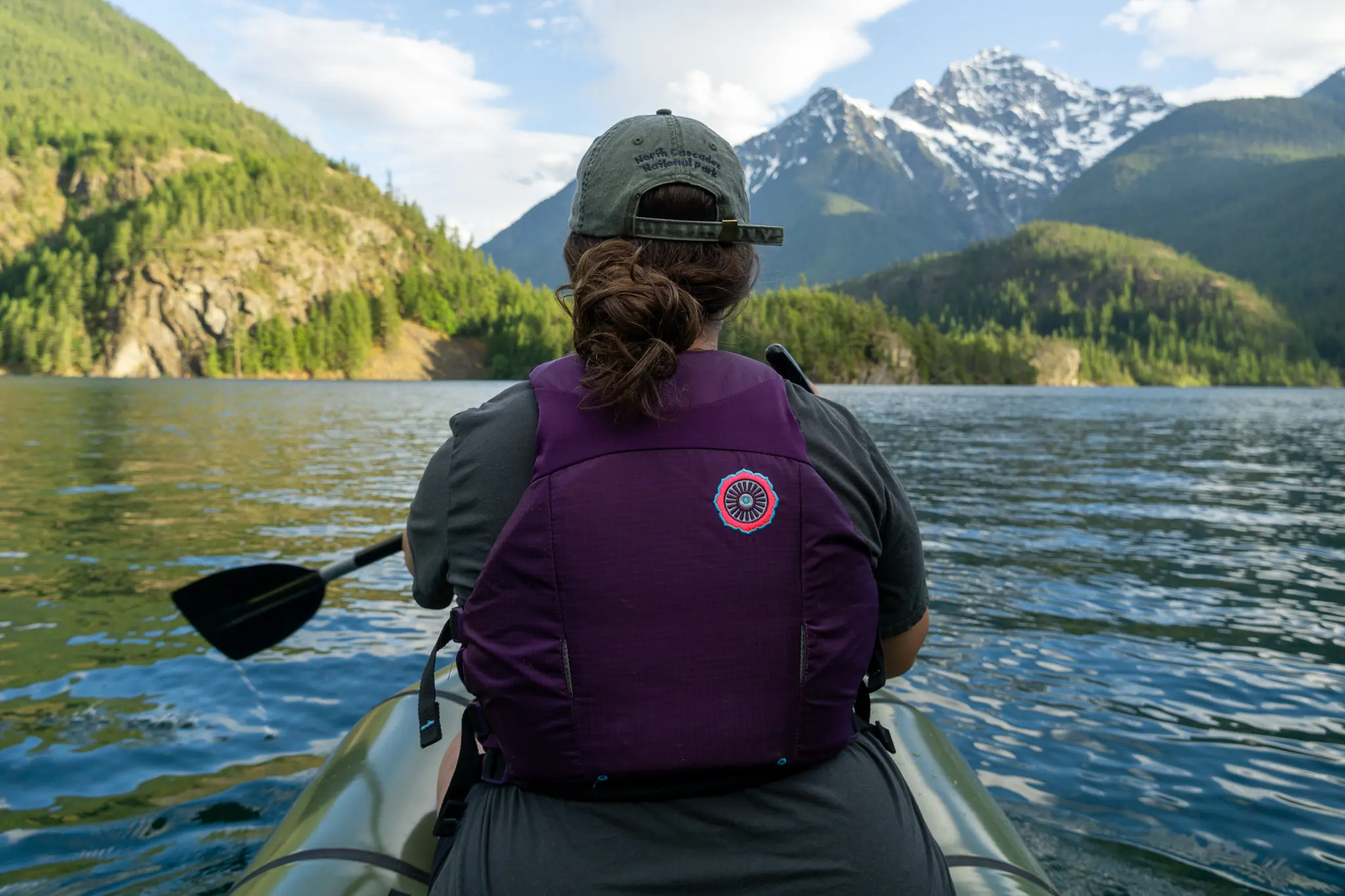 a woman in a purple pfd paddles the rendezvous looking across diablo lake