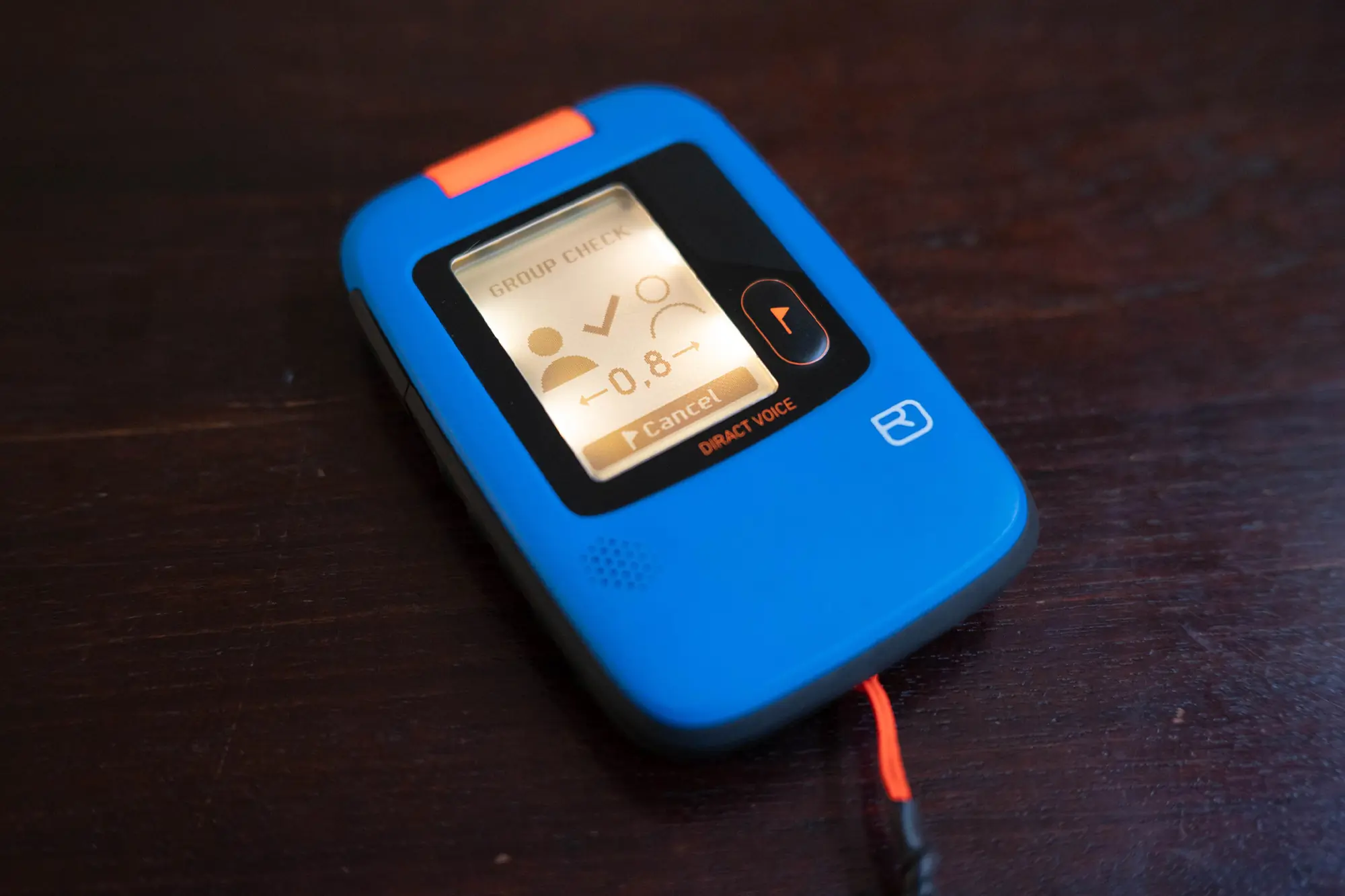 Blue avalanche beacon showing group check mode on a wooden surface