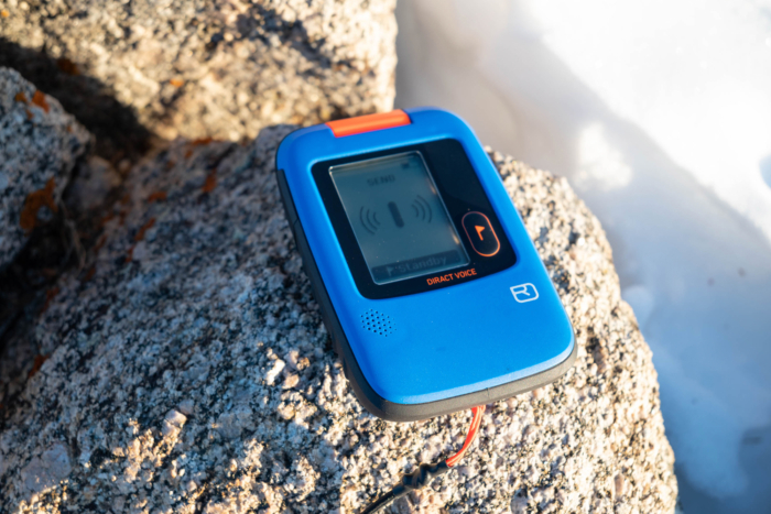 Blue avalanche beacon resting on a sunlit rock near snow