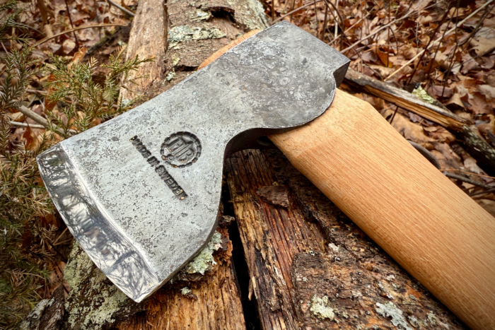 Close-up of the Hults Bruk Spika axe head resting on a mossy log, showcasing its forged steel and engraved logo