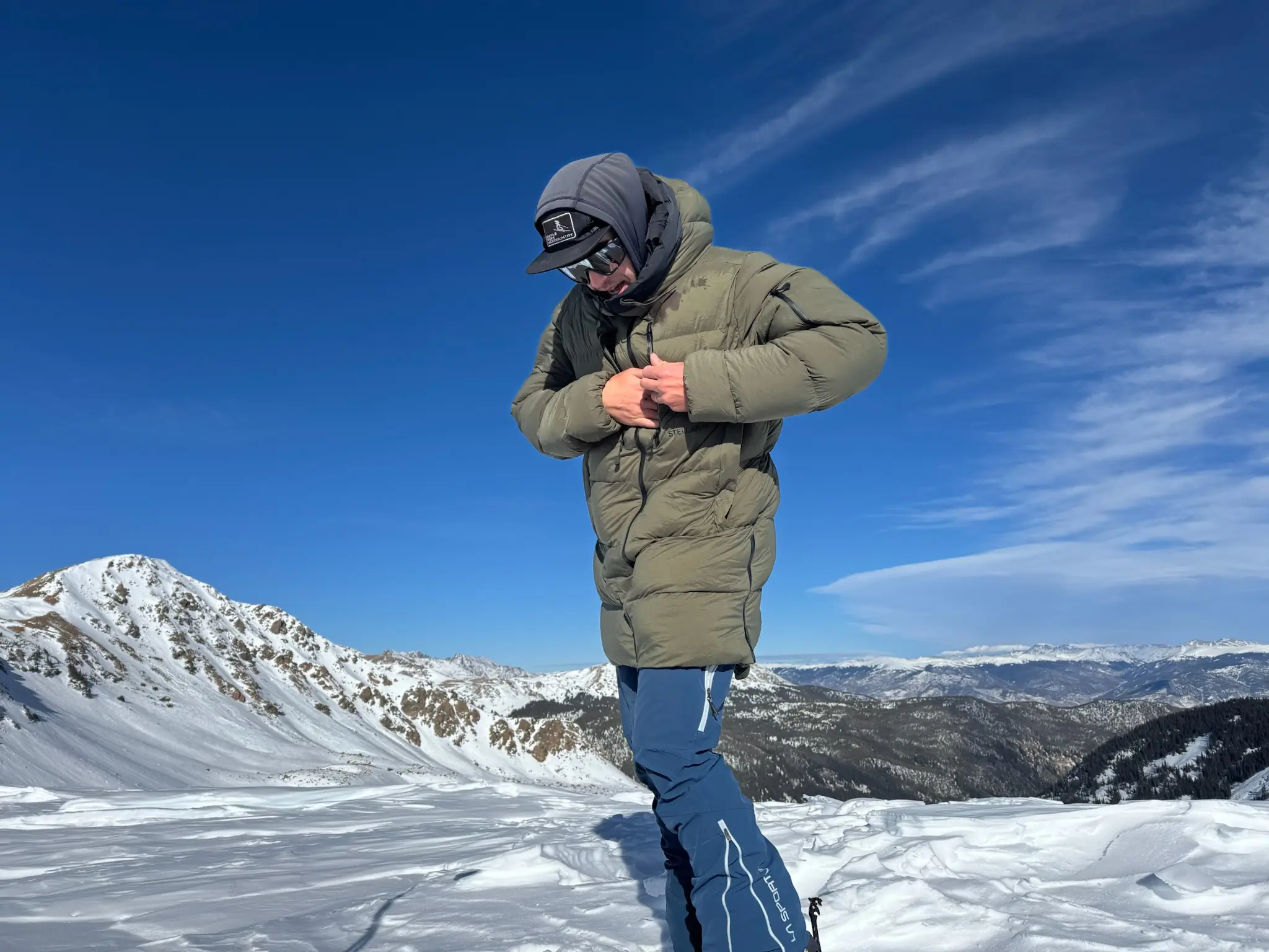 Person adjusting the Stellar Free Down Parka on a snowy mountain ridge