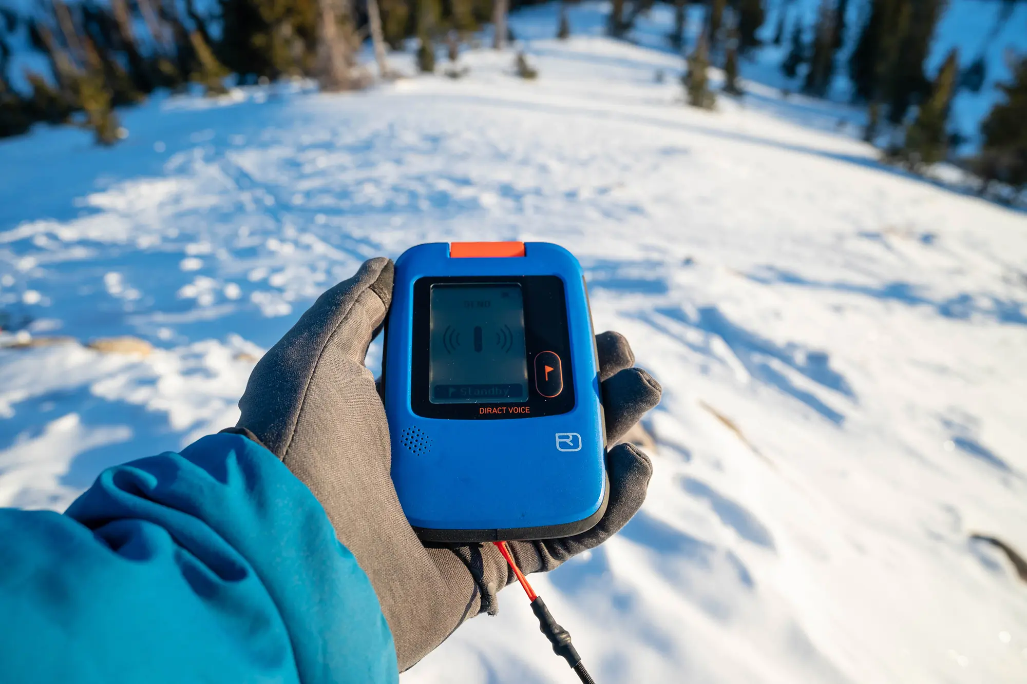 Ortovox Diract Voice beacon in use, held in a gloved hand over snowy terrain