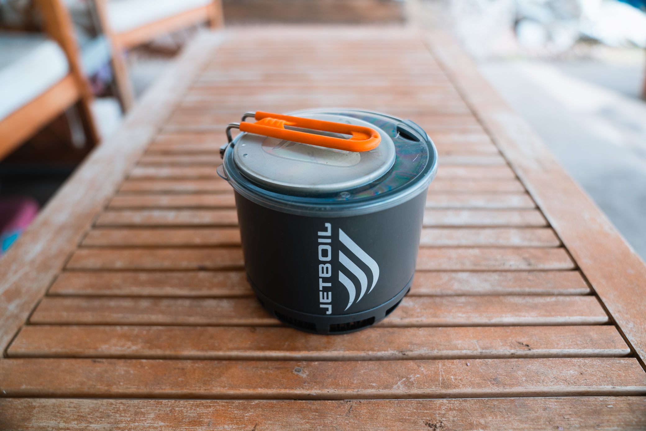 A compact Jetboil Stash stove with its lid secured and handle folded, sitting on a wooden table