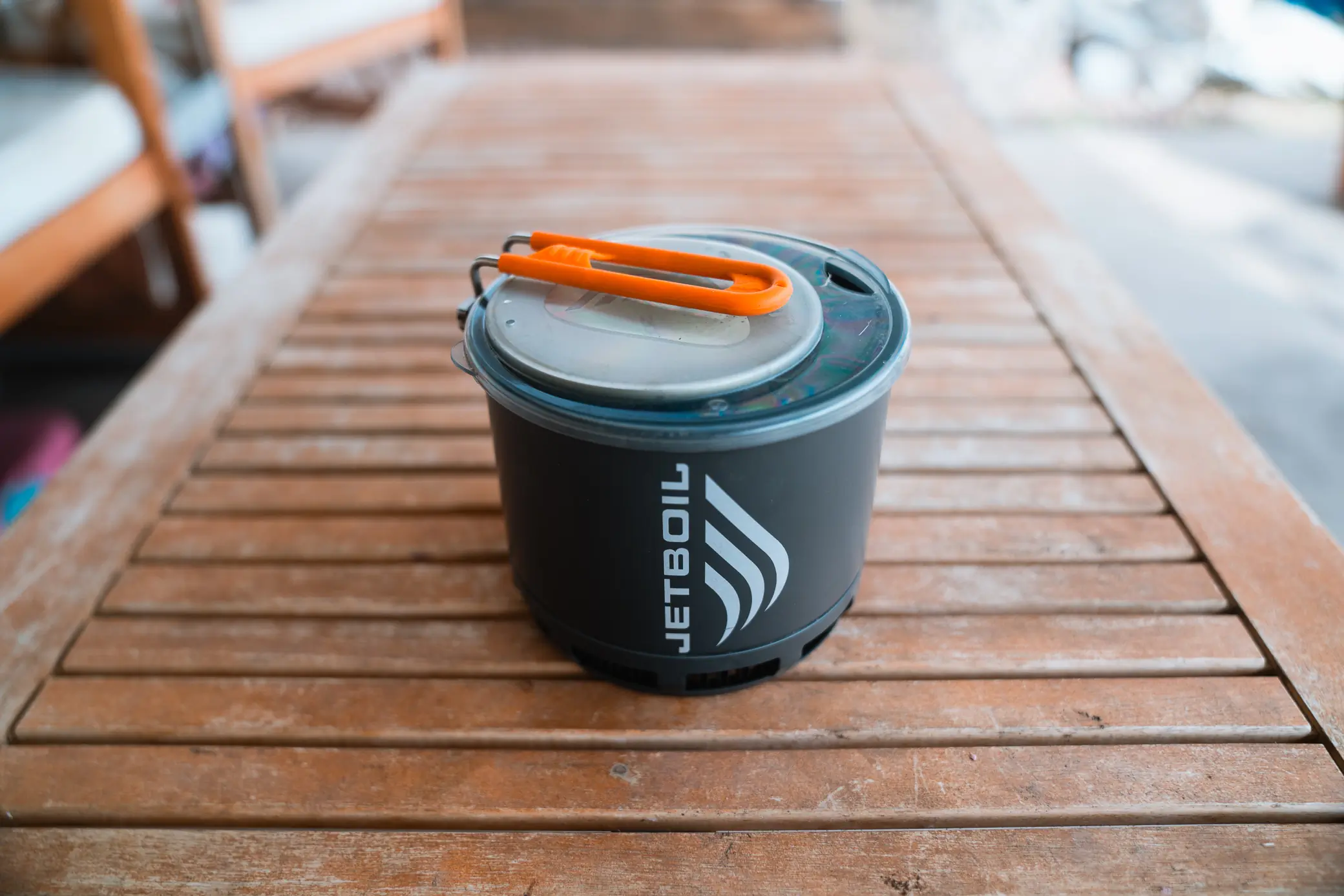 A compact Jetboil Stash stove with its lid secured and handle folded, sitting on a wooden table