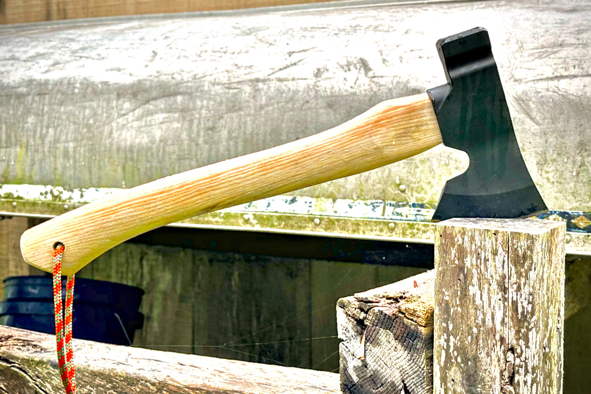 The Hardcore Hammers Camp Companion Axe balanced on a weathered wooden post, with a rugged outdoor background
