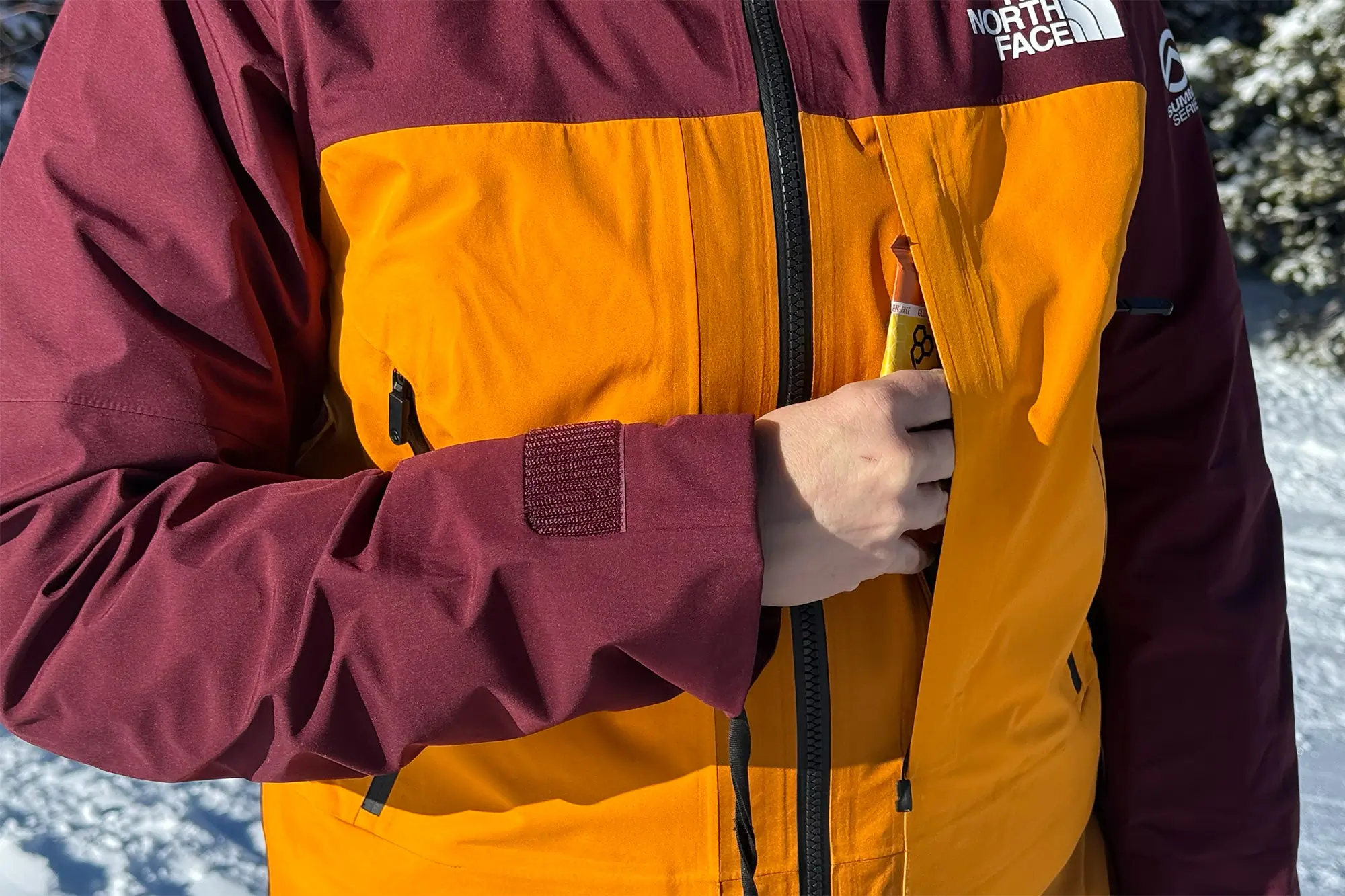A close-up of The North Face Summit Series Verbier Gore-Tex Jacket highlighting its large chest pocket, shown storing a snack bar, demonstrating its practical storage capacity