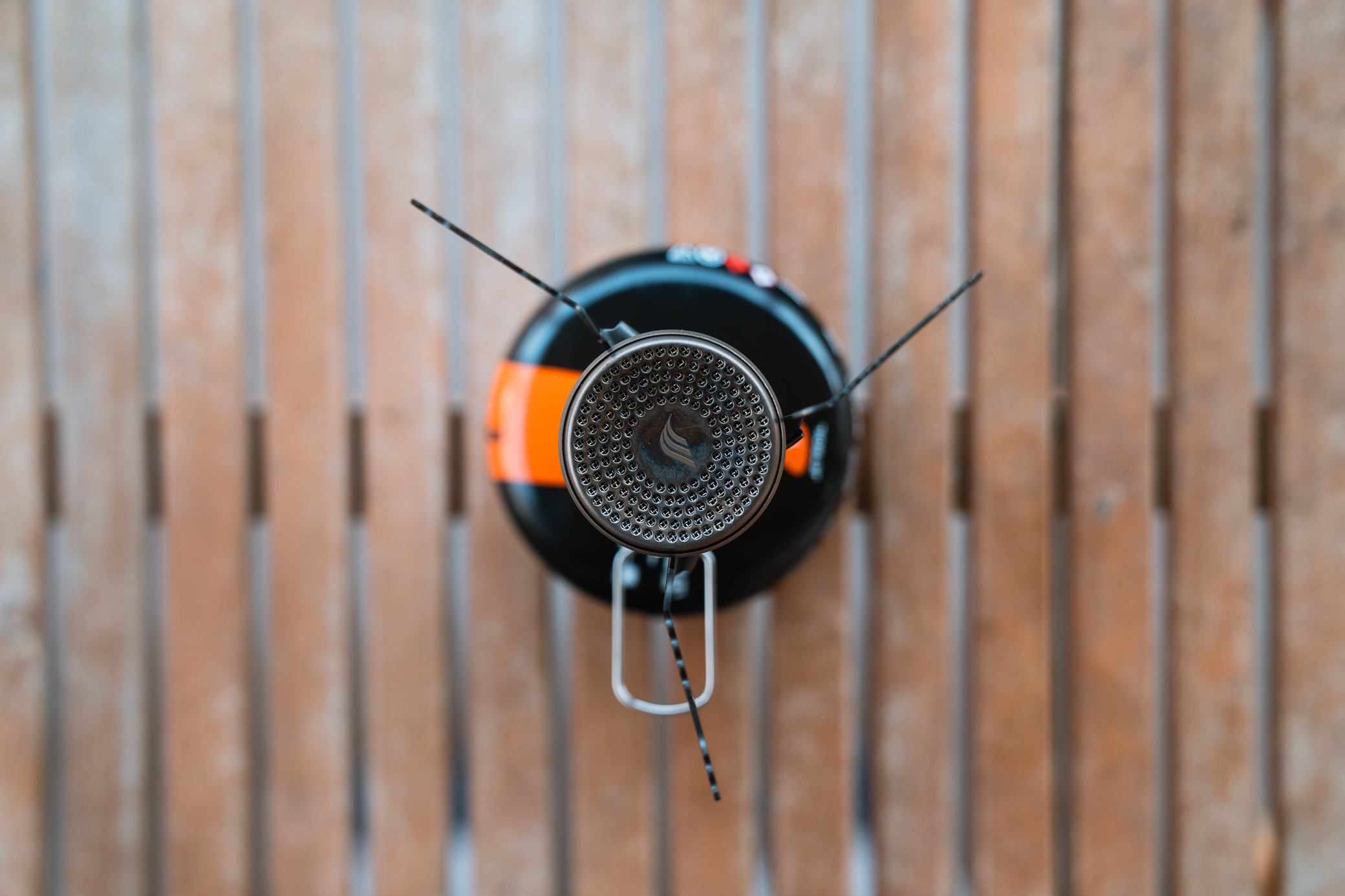 A top-down view of the Jetboil Stash stove burner with its pot supports extended, sitting on a wooden surface