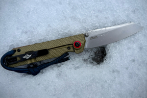 The OKNIFE XEN-OAL knife open on fresh snow, highlighting its sleek blade and textured handle