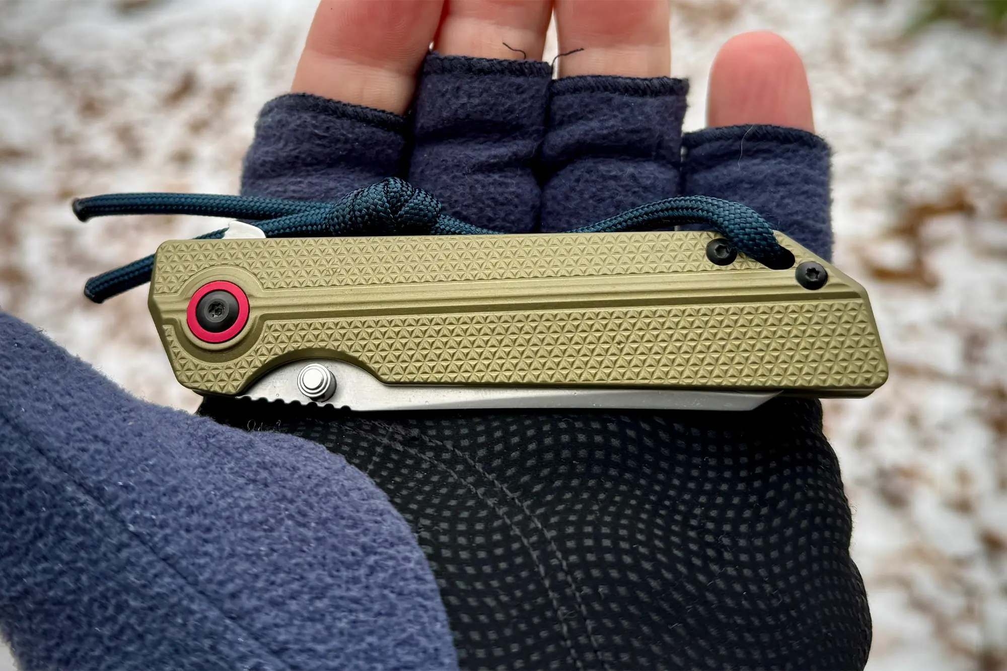 The knife in a folded position placed on a gloved hand, showcasing its compact size and textured grip