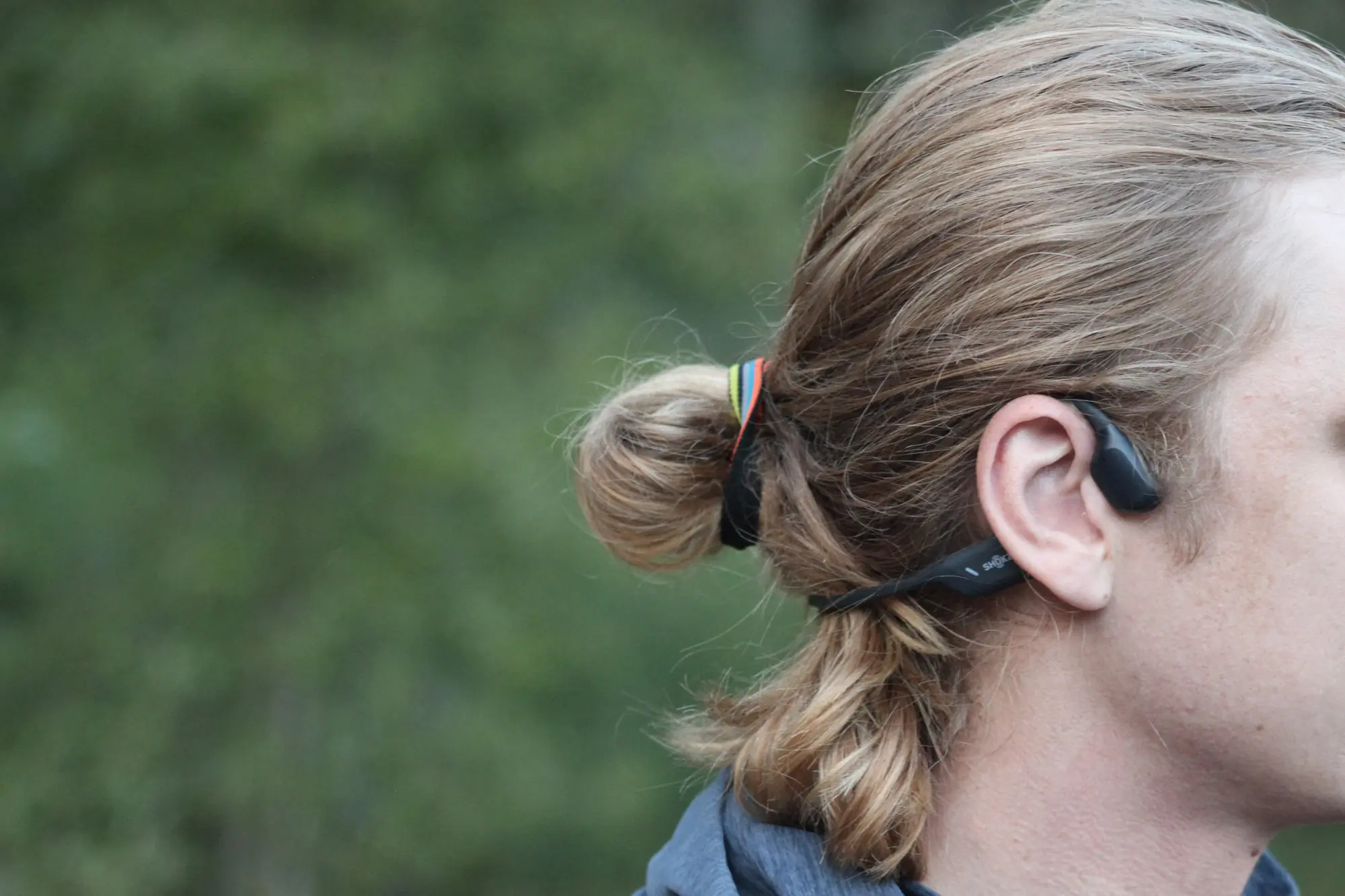 a runner wearing the shokz headphones shows the relative fit behind the ears