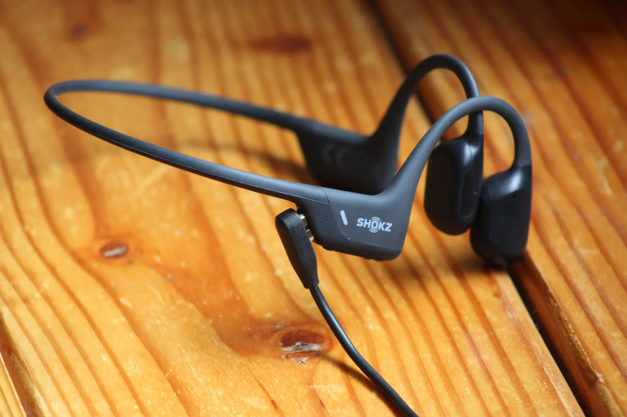 A detail image of the Shokz headphones connected to a charging cable